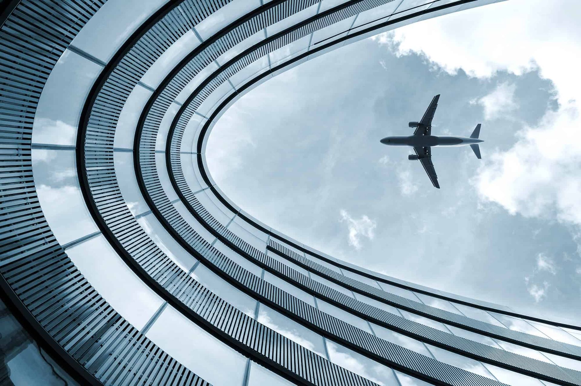 Góc nhìn từ dưới lên của một chiếc máy bay đang bay trên bầu trời, được bao quanh bởi kiến trúc hiện đại uốn cong