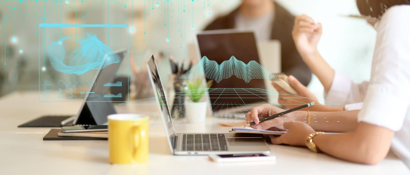 Nhóm người ngồi cùng bàn làm việc trên laptop, tablet với các biểu đồ ảo xuất hiện phía trên thiết bị – biểu tượng cho phân tích thiết kế hạ tầng giao thông nâng cao bằng OpenRoads Designer.