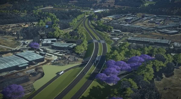 Nhìn từ trên cao đường cao tốc đi qua rừng và các tòa nhà công nghiệp, hàng cây tím tô điểm, minh họa sự kết hợp hài hòa giữa thiên nhiên và hạ tầng nhờ OpenRoads ConceptStation.