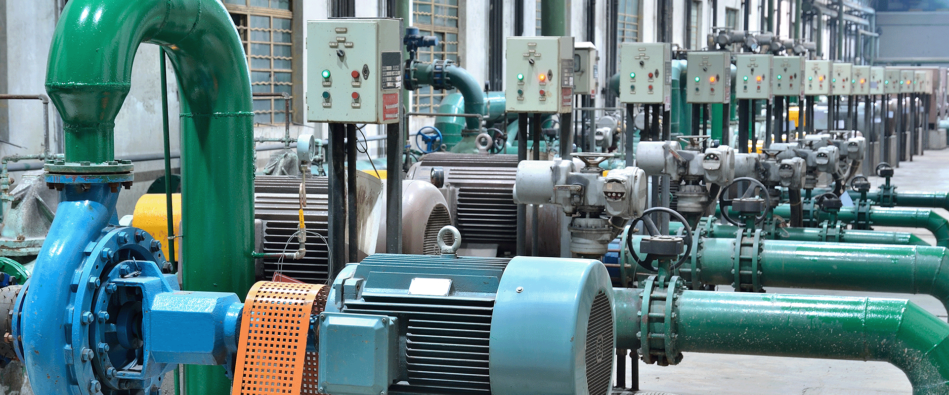 Dãy thiết bị bơm công nghiệp và động cơ cùng ống dẫn màu xanh lá và bảng điều khiển trong nhà máy, minh họa hạ tầng cấp nước bền vững được thiết kế tối ưu giảm chi phí năng lượng.