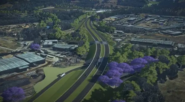 Nhìn từ trên cao đường cao tốc đi qua rừng và các tòa nhà công nghiệp, hàng cây tím tô điểm, minh họa sự kết hợp hài hòa giữa thiên nhiên và hạ tầng nhờ OpenRoads ConceptStation.