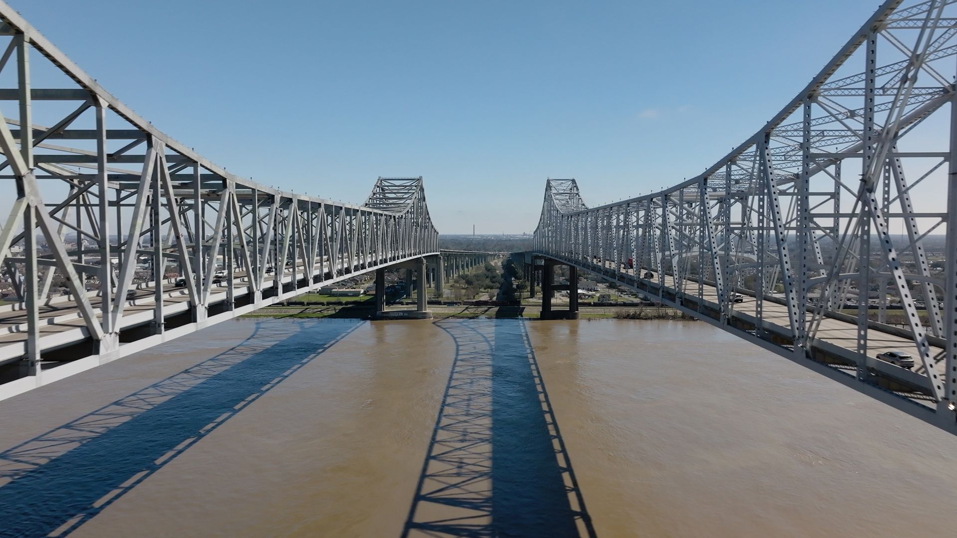 Hai cây cầu thép song song bắc qua dòng sông Mississippi tại New Orleans dưới trời xanh trong, mặt nước phản chiếu hình ảnh cây cầu.