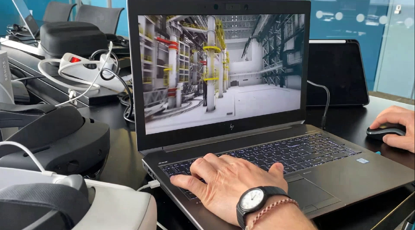 Một người thao tác trên laptop hiển thị mô hình 3D thiết bị công nghiệp, xung quanh là các thiết bị điện tử trên bàn.